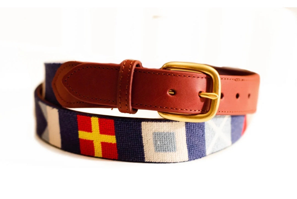 Navy needlepoint belt with colorful nautical flags, brown leather detailing, and a gold-tone buckle